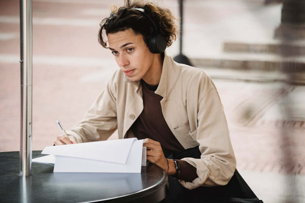 male wearing headphones writing with a pen and paper